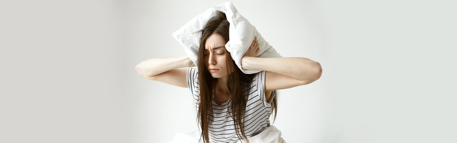 Girl covering ears with pillow to avoid snoring noise.